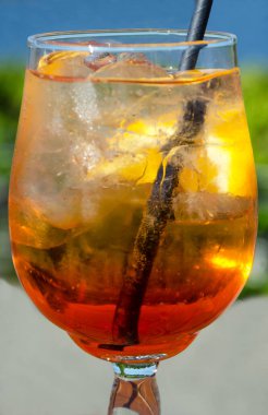 Bir bardak parlak turuncu Aperol Spritz kokteyli yaz yeşilliğinin arka planına karşı. Parlak bir portakal dilimi ve buz ile süslenmiş..