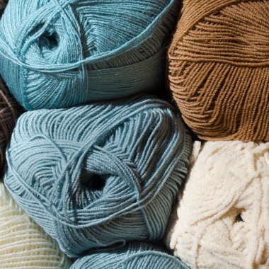 Mavi, kahverengi ve açık bej tonlarında iplik topları koleksiyonu. Sıkıca bükülmüş iplikler ve ipliğin yumuşak dokusu görülebilir..