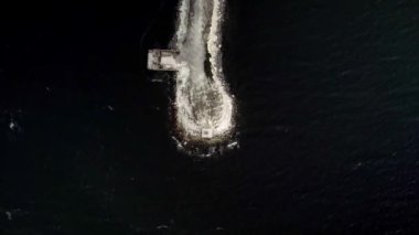 Dalgakıranın kuş bakışı görüntüsü. Balıkçı iskelesinde yürüyen insanlar. Koyu denizin ortasında kayalara vuran beyaz dalgalar. Statik kameralar insansız hava aracı görüntülerini düşürdü. Malmö, Limhamn, İsveç Bakış açısı Oresundsbron