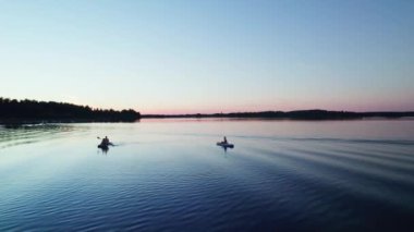 Anne, oğul ve kız gölde oturup şişme yemek tahtalarında kürek çekiyorlar. Dolly 'nin düşük açılı görüntüsü. Yaz ortası mavi saatinde aktif yaz tatili. Nas bruk, Dalarna İsveç