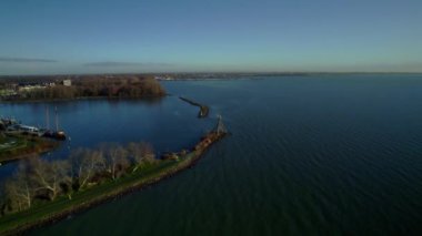 Flying over the coastline with wooden harbor light and a beacon licht at the bay entrance, lighthouse of the harbor in Hoorn the Netherlands. Morning during winter, high angle aerial view