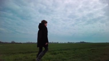 Ciddi düşünceli bir yürüyüş çocuğu, doğa yürüyüşçüsü kırsal manzara, dramatik bulutlar. Uzağa bakan yalnız çocuk. İnsanlar ve çevre konsepti Düşük açı sağ taraf görünümü yavaş çekim