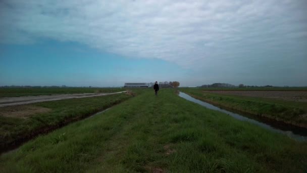 スローモーションのフロントビューでは 9歳の子供だけで溝と牧草地の間の芝生の堤防の歩道を歩く 背景の農場 曇りの日と青空 — ストック動画
