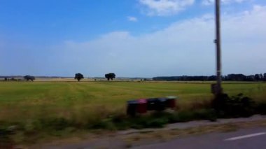 Side view from car window of green countryside, round hay bales on the fields. Blue sky and clouds in summer sunny day on Sweden. Trip and travel by car concept.