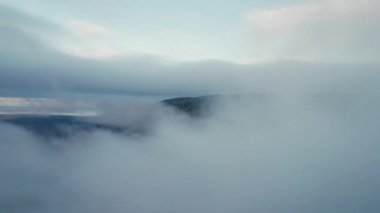 Dik kayalık dağ uçurumunun yan manzaralı alçak asılı bulutların üzerinde uçmak, rüya gibi atmosferik bulutlar. Sabahları İskandinav topraklarında beyaz kabarık bulutlarda yüzen drone.