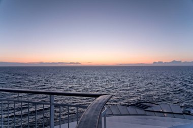 Dalgalı deniz manzarası ve yolcu gemisinin kıç güvertesinde güzel bir turuncu ve mavi akşam gökyüzü. Yaz tatili kavramı