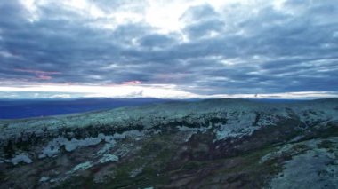 Kaygan dağ sırtı yamacı boyunca kayan kayalıklar ve arka planda dağlar. Yaz günbatımında canlı ve renkli akşam gökyüzü olan bulutlu manzara, İskandinav doğası