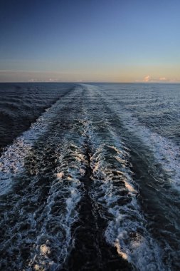 Kuzey Norveç 'in boş, soğuk ve su izi olan deniz manzaralı yolcu gemisi. Dalgaların düz çizgisi ve güneş doğmadan önce beyaz köpük, mavi turuncu sabah gökyüzü. Tatil ve seyahat kavramı