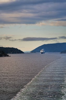 Norveç 'teki gemi, dağ ve ormanlarla birlikte Oslofjord' un kıç güvertesinden görüntüyü alıyoruz. Dalgalardan ve beyaz köpüklerden oluşan su izlerini uyandır, mavi-turuncu sabah gökyüzü. Tatil ve seyahat kavramı