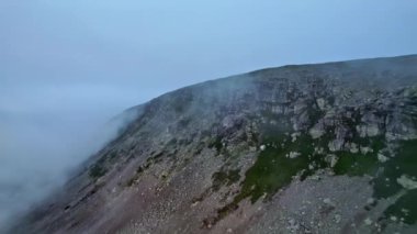 Hava, yeşil yosun, gri kaya oluşumları ve sis ile keskin uçurumlar vurdu. Geri geri uçmak dağ sırtı açığa çıkarmak. Mavi şafak bulutlu hava ve gün doğumu kuzey doğada