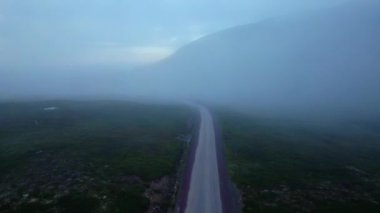 Terk edilmiş çakıl yollarının üzerinde uçarak tundra manzarası boyunca bulutlarla çevrili bir dağ boyunca İskandinav doğası bölgesinde gizemli sisli bir sabah boyunca.