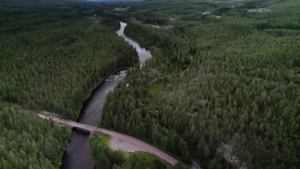 川を渡る橋で駐車された車の空中ビュー スウェーデンの緑のスプルースの森を介して川と風の国道の上の映画のドローンショットムーブメント — ストック動画