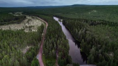 Nehir kıyısındaki köprüde park halindeki aracın hava görüntüsü, nehir üzerinde sinematik dron görüntüsü ve İsveç 'teki yeşil ladin ormanından geçen arabayla dolambaçlı kır yolu.