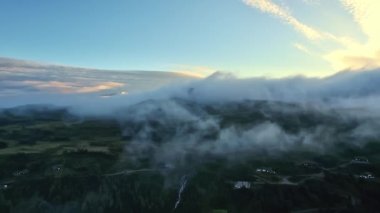 Hava manzarası, bulutların üzerinde uçan insansız hava aracı. Boreal ormanı, kır evleri ve dağ deresi, sisle kaplı dağ sırtı. Norveç 'in doğal manzarasına kuşların bakış açısı