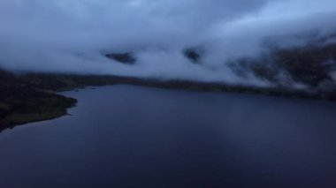Gece güzel mavi bir göl üzerinde uçarken, sahildeki tatil kulübelerinde, dağlara karşı ışıklar ve İskandinavya 'daki alçak bulutlarla, Drone Dolly 4K çözünürlüğü vurdu.