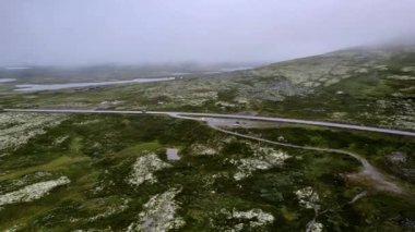 Park yeri ve dinlenme yerinde park halindeki arabalarla hava yörüngesi çekimi. Yoğun sisli dağ manzarası Rondane Ulusal Parkı Norveç 'te yol gezisi, liken, ren geyiği yosunu ve göletli çorak kayalık bölge