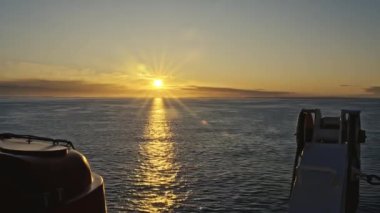 Sancak tarafında güneş doğuyor. Yolcu gemisinden filika ve davit vinçle. Altın sabah güneşi sakin dalgalarla yüzeyde yansıyor. Ufukta Norveç kıyılarında, seyahat kavramı