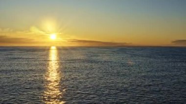 Deniz kenarında güneş güvertesinden altın gün doğumu. Sabah güneşi, güneş ışınları ve mercek parıltısı deniz yüzeyine sakin dalgalarla yansıyor. Ufukta Norveç kıyılarında yelken seyahati konsepti