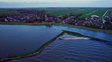 Mavi Markermeer Gölü, Hollanda 'nın Schellinkhout köyü, evleri, kilisesi, çiftlikleri ve su baskınlarına karşı korunmak için Levee' nin arkasındaki otlakların su altında kalmış plajı ve altyapısının hava görüntüleri.