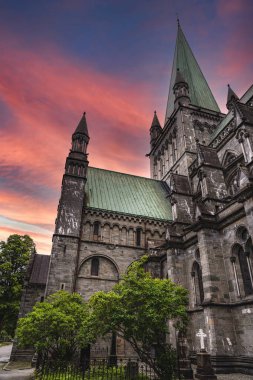 Norveç 'in Trondheim kentindeki Nidaros Katedrali üzerinde gün batımı parıltısı. Katedral, gün batımının canlı renklerinde güneşleniyor. Gökyüzünün Gotik mimarisi akşam arkaplanına vurgulanıyor.