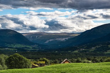 Norveç 'teki sakin Oppdal Vadisi' ne akşam çöküyor. Çiftlik çatıları yamacın hemen üstünde zirveye ulaşıyor ve sizi vadi sahnesine götürüyor. Dağlar manzarayı kucaklıyor.