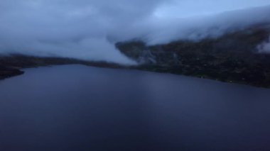 Dağların üzerinde alçak asılı bulutlarla Norveç Gölü 'nün karanlık hava kayması görüntüsü. Aydınlatılmış kır evleri Oppdal, Trondelag Norveç 'te akşam boyunca manzarayı noktalıyor.