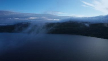 Sakin bir göl üzerinde bulutların üzerinden uçan dağ sırtı alçak bulutlarla örtülmüş, son gün ışığıyla birlikte Norveç 'in pitoresk bir vadisinde akşam çöküyor..