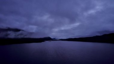 Oppdal, Trondelag Norveç 'teki Skarvatnet Gölü üzerinde manzaralı bir gece uçuşu. Koyu dağlar beyaz bulutlara karşı duruyor Keskin bir siluet oluşturuyor.