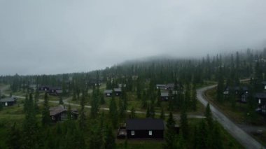 Norveç, Sjusjoen 'deki lüks kayak kulübelerinin hava manzarası, karanlık, yağmurlu bir yaz akşamında sisli dağlarla ve Nimbostratus bulutlarıyla çevrili..