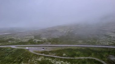 Norveç 'in Venabygd yakınlarındaki Rondane Ulusal Parkı' ndaki yeşil tundranın üzerinde uçarak puslu doğa manzarasını gösteriyor ve bulutlu dağlarda kayboluyor.
