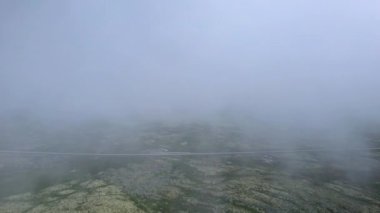 Cladonia yosunlu tundrasını, park etmiş arabaları ve Norveç 'teki Rondane Ulusal Parkı' ndaki dalgalı bir dereyi gösteren sisli bir dağ yamacının üzerinden uçuyoruz..