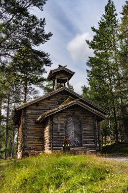 A small wooden mountain chapel stands amidst tall pine trees in the Swedish forest, a Christian cross visible on its exterior in Idre Dalarna