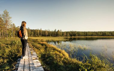 Akşam güneşi Idre Dalarna İsveç 'in manzarasına sıcak bir parıltı saçarken, sakin bir göle bakan tahta bir kaldırımda duran kadın.