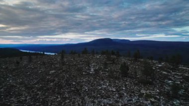 İnsansız hava aracı dağın tepesinde uçuyor ve alacakaranlık gökyüzünün altındaki yemyeşil ormanların arasına kurulmuş sakin bir gölü ortaya çıkarıyor. Idre Dalarna, İsveç 'in dingin güzelliğini tecrübe edin.