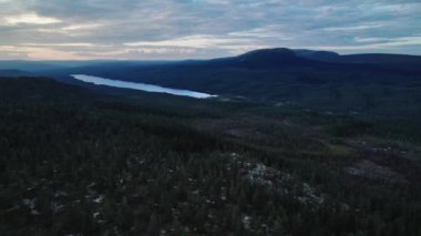Nefes kesici hava perspektifi, Dalarna İsveç 'in üzerinde güneş batarken yoğun ormanlar ve dağlarla çevrili sakin bir göl yakalar ve doğada sakin bir atmosfer yaratır. İHA geriye doğru uçuyor