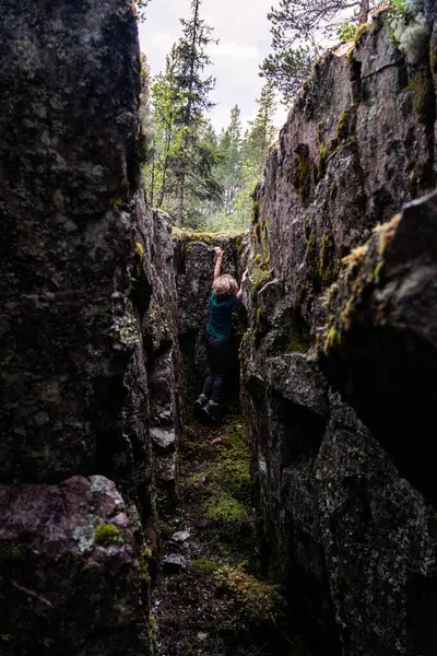 Küçük bir çocuk İsveç 'te yüksek ağaçlar ve yosun kaplı kayalarla çevrili dar bir kaya kanyonuna tırmanıyor. Atmosfer, uzak bir doğal ortamda maceraperest bir keşif olduğunu gösteriyor..
