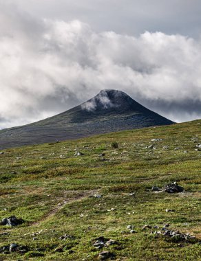 İsveç 'in Idre Dalarna kentindeki Stadjan dağının çarpıcı tundra manzarasını keşfedin. Yeşil tepeler ve bulutlarla kaplı görkemli bir tepe.