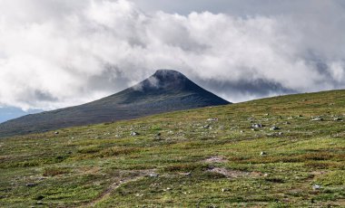 İsveç 'in Idre Dalarna kentindeki Stadjan dağının çarpıcı tundra manzarasını keşfedin. Yeşil tepeler ve bulutlarla kaplı görkemli bir tepe.