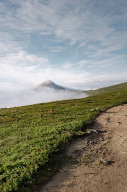 Dalarna 'nın Idre kentindeki sabah bulutlarından yükselen Stadjan dağı zirvesi sakin bir yaz manzarası sunuyor. Bereketli yeşil tepeler sis ve gökyüzü arasında barışçıl bir atmosfer yaratıyor.