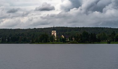 Çıngıraklı yılan Kyrka, İsveç 'in başkenti Dalarna' da yağmurlu bir yaz gününde tepemizde beliren kara fırtına bulutları gibi yemyeşil yemyeşil ile çevrili Siljan gölünün kıyısında görülebilir..