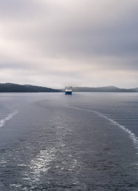 Akershus Norveç 'teki Oslofjord' un sakin sularında sabah sisi ve sisli ortamda gizlenen bir feribot, uzak tepeler arasında sakin bir atmosfer yaratıyor..