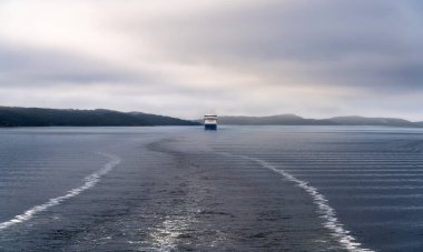 Akershus Norveç 'teki Oslofjord' un sakin sularında sabah sisi ve sisle örtülü bir gemi, uzak tepeler arasında sakin bir atmosfer yaratıyor.