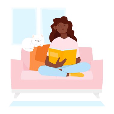 Koyu tenli genç bir kadın kanepede oturup kitap okuyor.