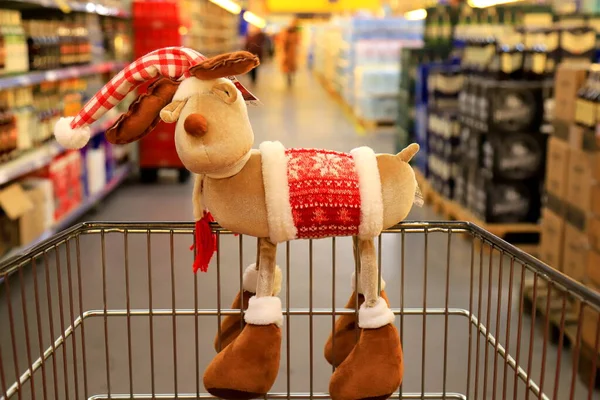Christmas, New Year sale, shopping. Funny Christmas deer on supermarket trolley. Basket in wholesale store, background of blurred groceries and goods.