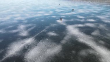 Kışın buz nehri. Balıkçılar nehirde donmuş güzel mavi buzda avlanıyor, kışın göl, yukarıdan insansız hava aracı manzarası.