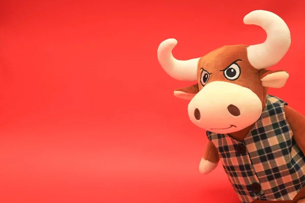 Funny toy orange bull on a red background. Beautiful bull with big white horns, space for text