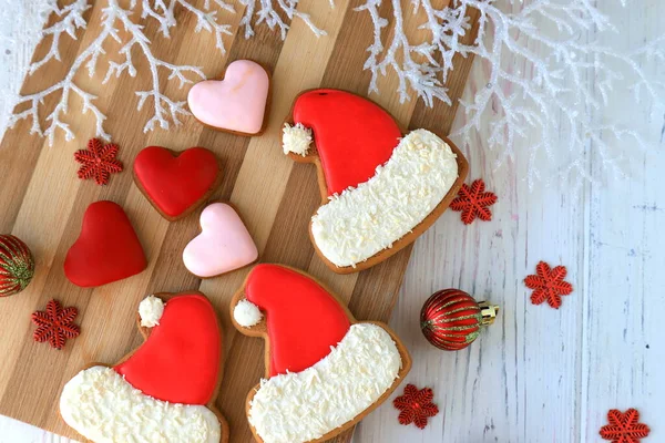 Christmas New Year food, sweet gingerbread cookies in form of Santa Claus cap and heart lie among New Year decorations on wooden background