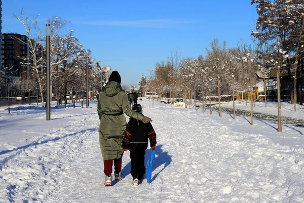People walk in winter along snow-covered street in warm jackets. Winter sports and recreation in city Dnipro, Ukraine