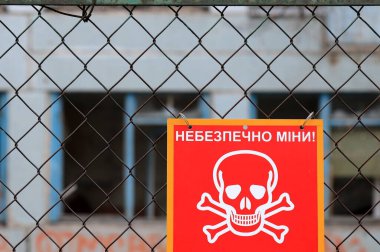 Danger mines - Red sign with inscription in Ukrainian, Skull and crossbones - sign of death from military mine against of destroyed building, Russia war against Ukraine, 2022-2023