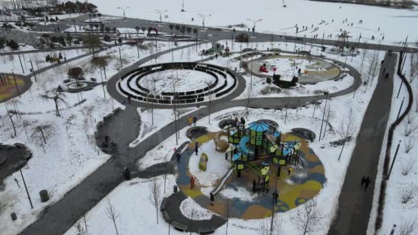 雪で覆われた子供の遊び場を持つウィンターパーク広場通り 子供と大人は冬にスライドとスイングに乗ります Dnipro ウクライナ ドローンからのトップビュー — ストック動画